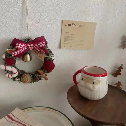 Christmas Gift Decorative Wreath for Home Decor hanging with a bell and festive decorations next to a Santa mug.